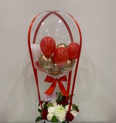 Transparent Balloon stuffed with 3 gold and 3 red balloons Tied with ribbons to a basket of 12 red and white flowers